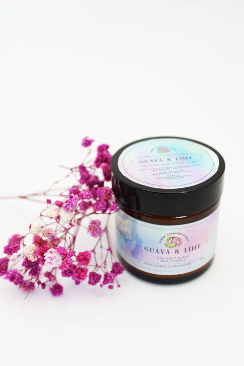 Brown glass candle with holographic sticker branding, with pink flowers on a white background